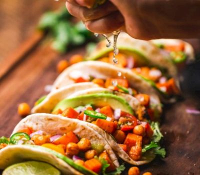 a hand pouring a liquid over tacos