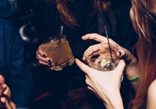 A group of people is enjoying drinks and engaging in conversation at a social gathering or party, with their hands shown holding beverages.