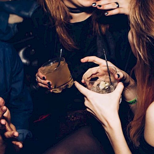 A group of people is enjoying drinks and engaging in conversation at a social gathering or party, with their hands shown holding beverages.