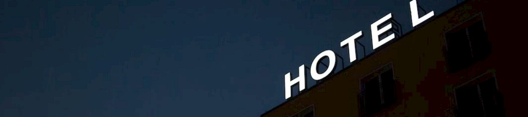 A building at night with an illuminated "HOTEL" sign is shown, but the "E" is dark, making it read "HOT L".