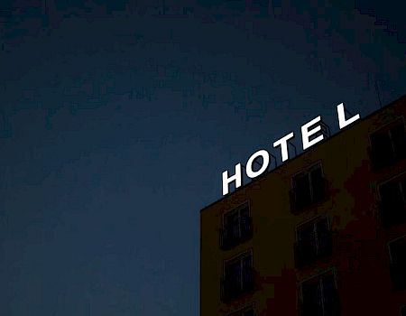 A building at night with an illuminated "HOTEL" sign is shown, but the "E" is dark, making it read "HOT L".