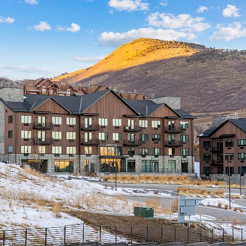 A large building with multiple windows stands in a snowy landscape, with a mountain in the background under a blue sky.