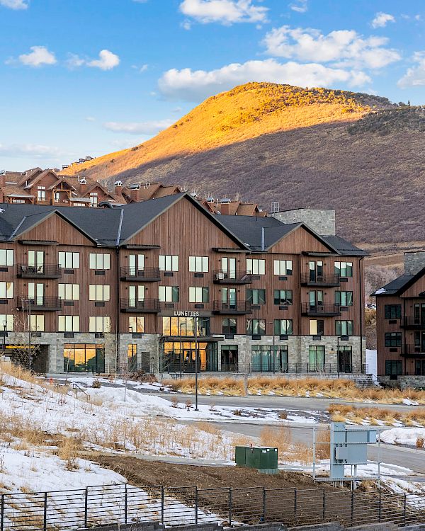 A large building with multiple windows stands in a snowy landscape, with a mountain in the background under a blue sky.