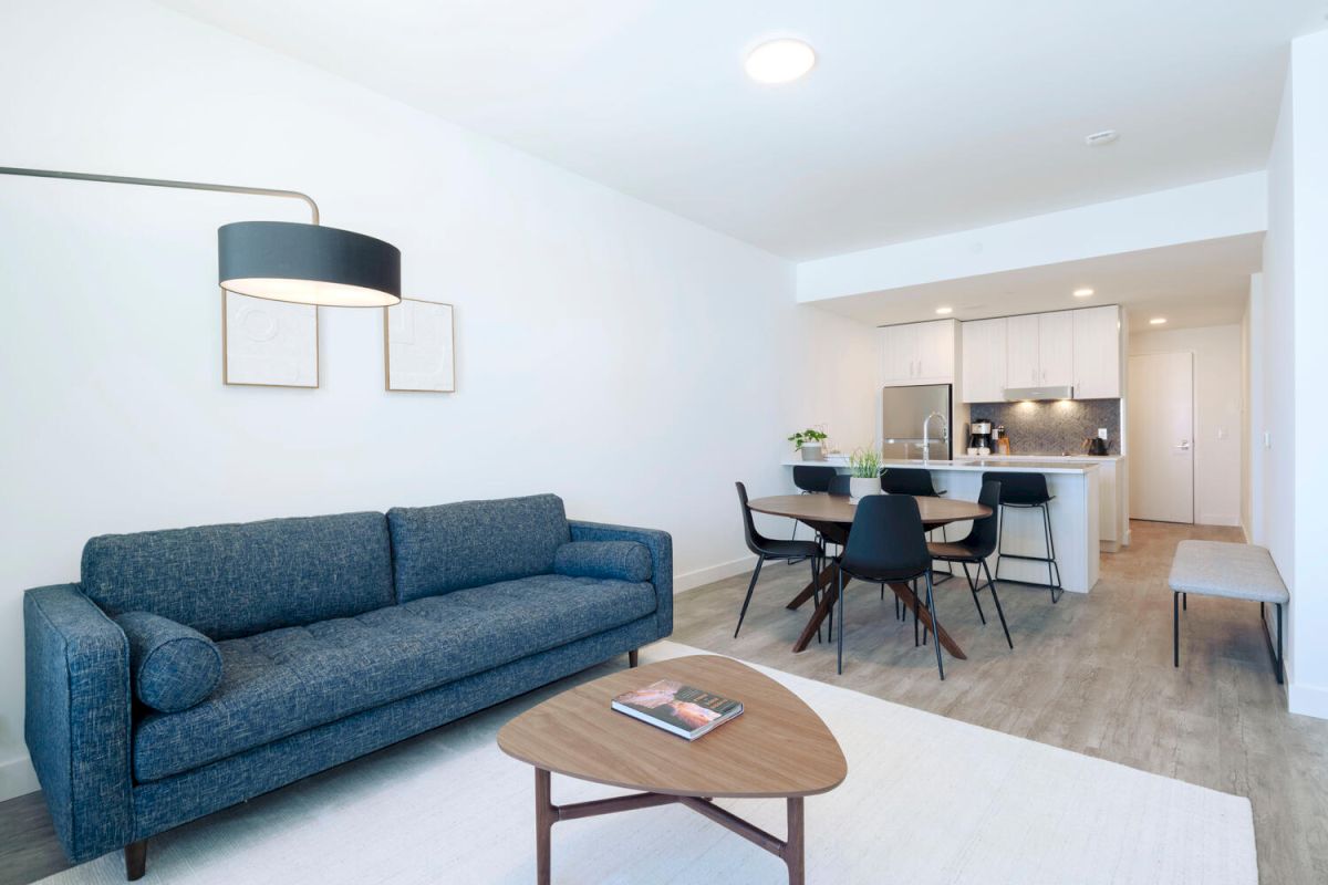 A modern living room with a blue sofa, wooden coffee table, and kitchenette in the background.