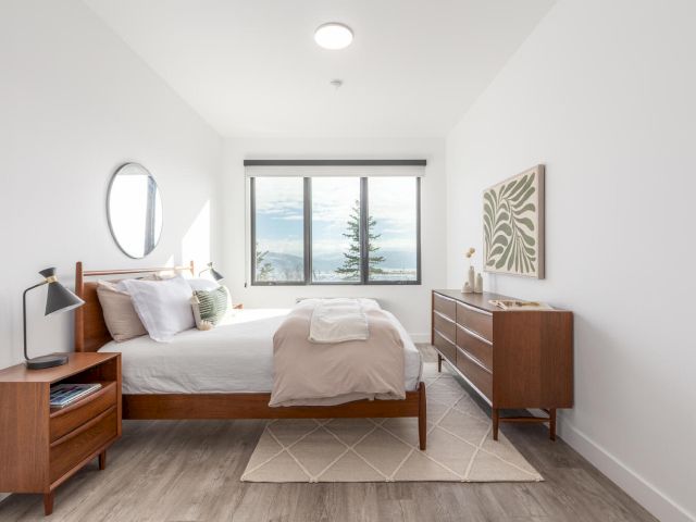 A wide view of a clean and minimalist guest room with a bed, dresser, and nightstand.