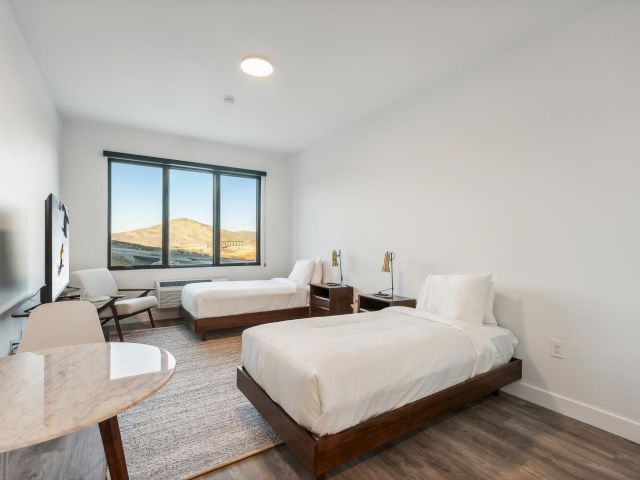 A hotel room with two beds, a desk, and a large window with a view of mountains.