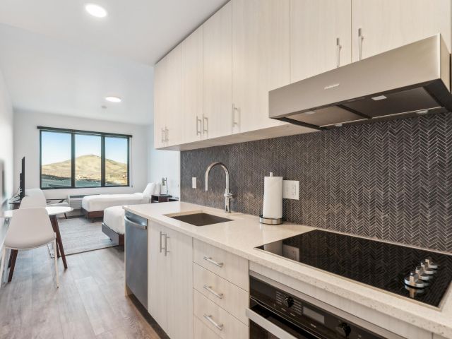 A modern kitchenette with a dining area and beds in the background.
