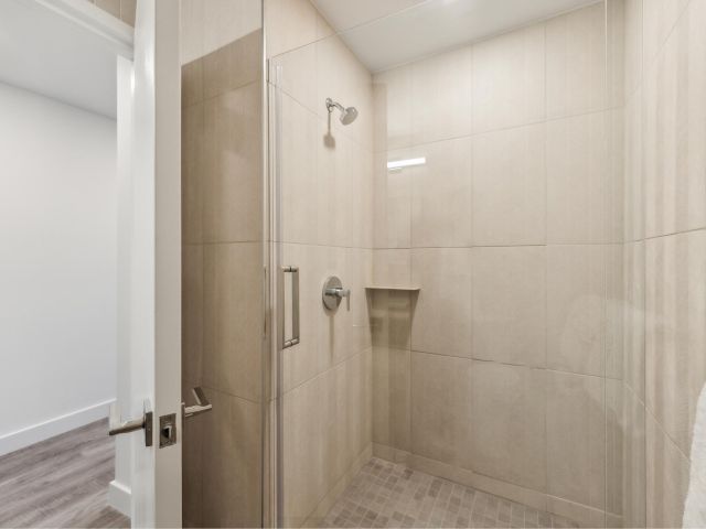 A modern bathroom shower with large beige tiles and a glass door.