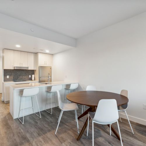 A modern kitchen and dining area with white cabinets, a round table, and white chairs on wood flooring.