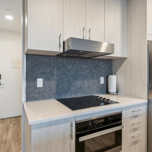 A modern kitchen with a stovetop, oven, stainless steel fridge, and herringbone tile backsplash. Bright and minimalistic design.