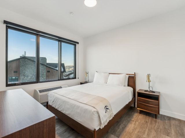 A clean and minimalist bedroom with a large window, a bed, and a desk.