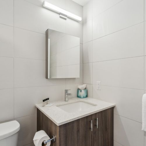 A modern bathroom with a toilet, sink cabinet, mirror, towel rack, and toilet paper holder on a bright, tiled wall.