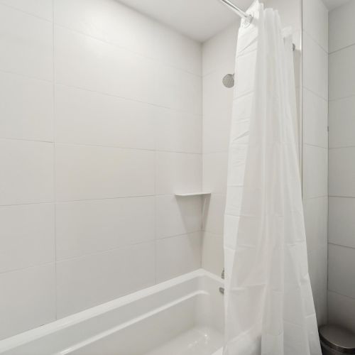 A white bathroom features a bathtub with a curtain, tiled walls, and a toilet.