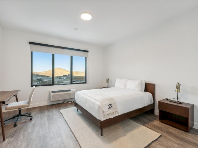 A clean and minimalist hotel room with a large bed, desk, and window showing a mountain view.