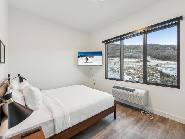 A hotel room with a bed, window, TV, and heater.