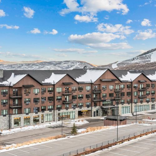 The image shows a large building with a snowy roof, set against a backdrop of snow-covered hills and a clear sky.