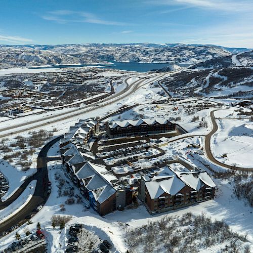 Aerial view of a snow-covered mountain resort town with winding roads, large buildings, scattered houses, and a lake in the background.