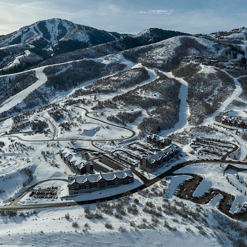 The image shows a snow-covered mountain resort with ski trails, buildings, roads, and surrounding mountainous terrain.