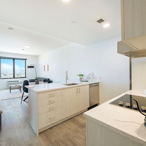 A modern kitchen and dining area with light wood cabinets, a center island, and a view of a windowed living space, ending the sentence.