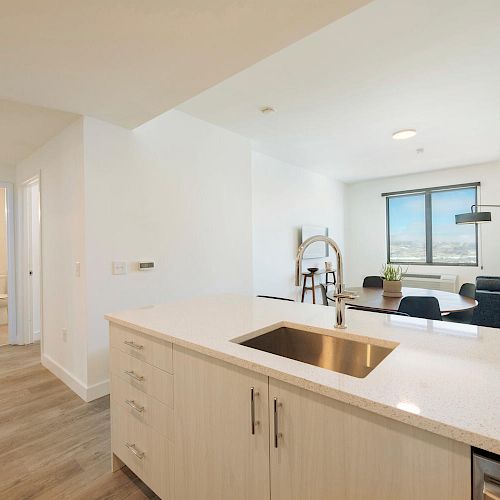 A modern apartment with an open kitchen, living area, and hallway leading to a bathroom. The kitchen features a sink and countertop.