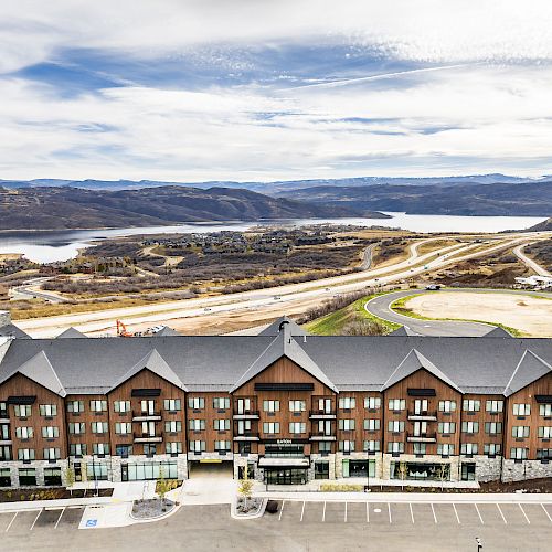 A large building with a scenic backdrop of hills, a winding road, and a body of water.