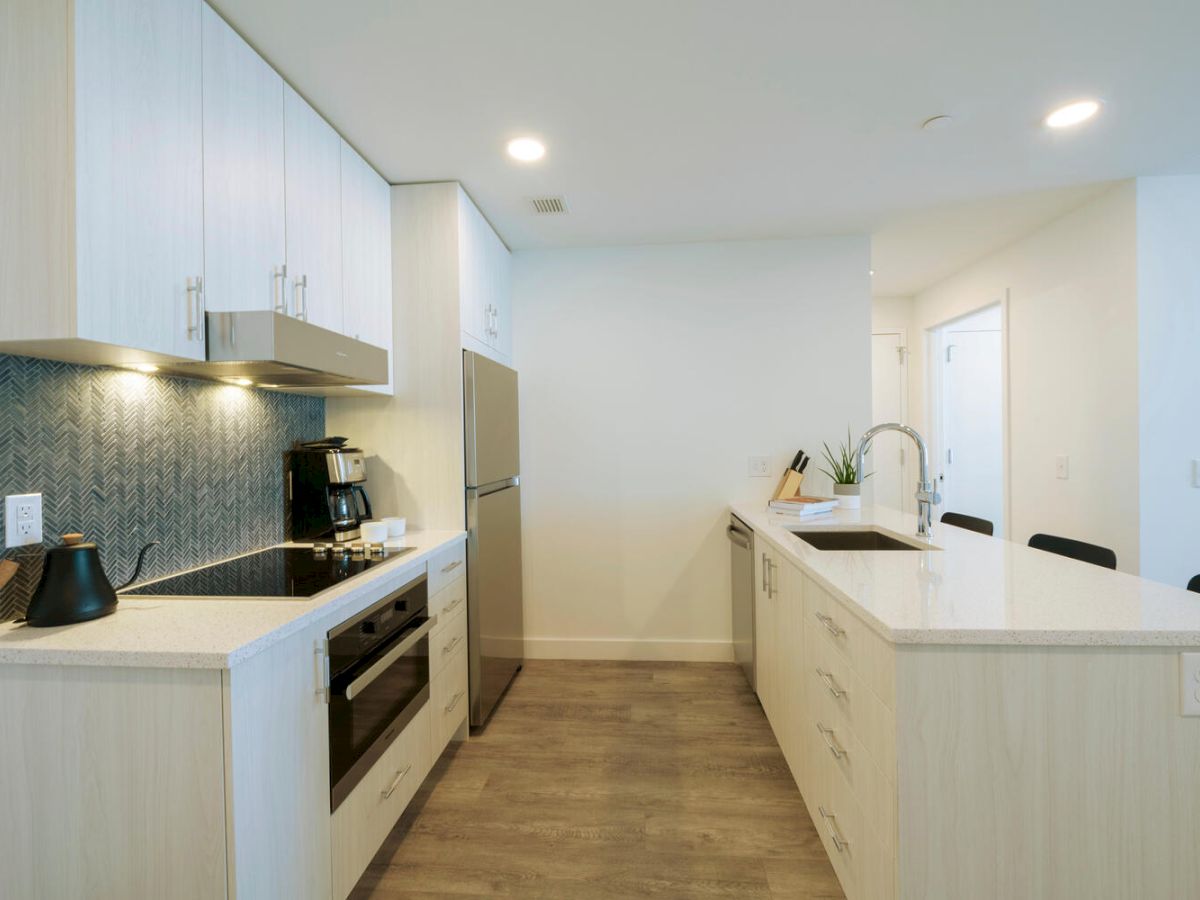 A modern kitchen with light wood cabinets, stainless steel appliances, a large island, a backsplash, and various kitchenware items.