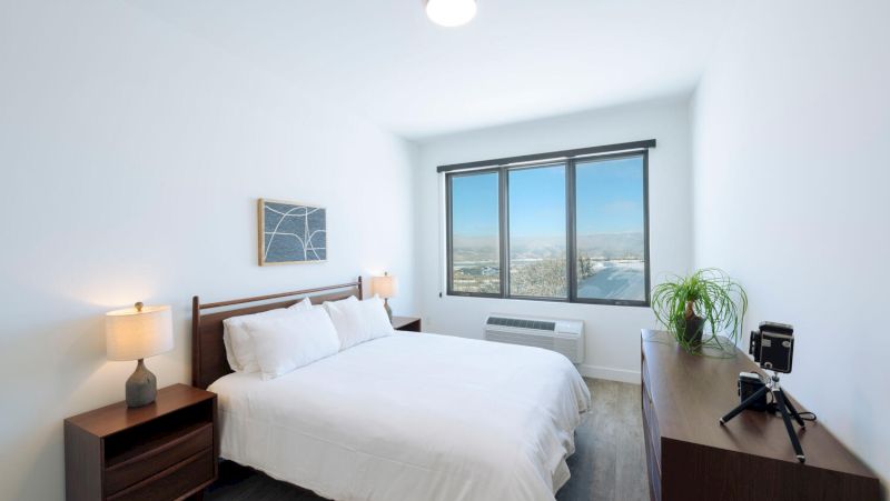 A clean and minimalist hotel room with a large bed, window, and city view.