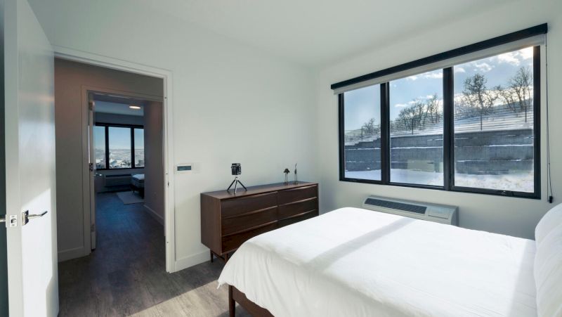 A wide-angle view of a hotel room with a bed, dresser, and doorway leading to another room.