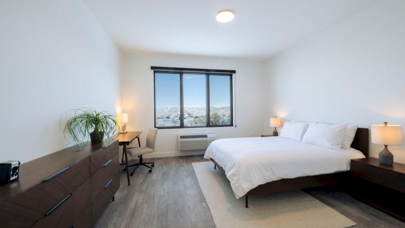 A clean and modern hotel room with a large bed, desk, and window.
