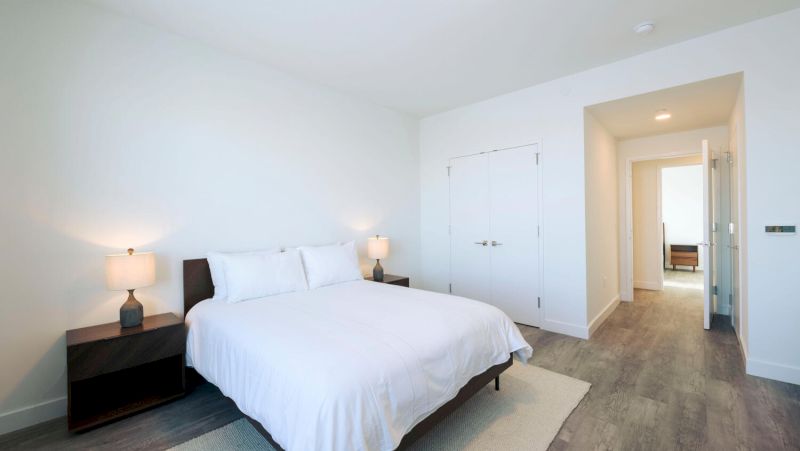 A hotel room with a bed, two nightstands with lamps, a closet, and a doorway leading to another room.