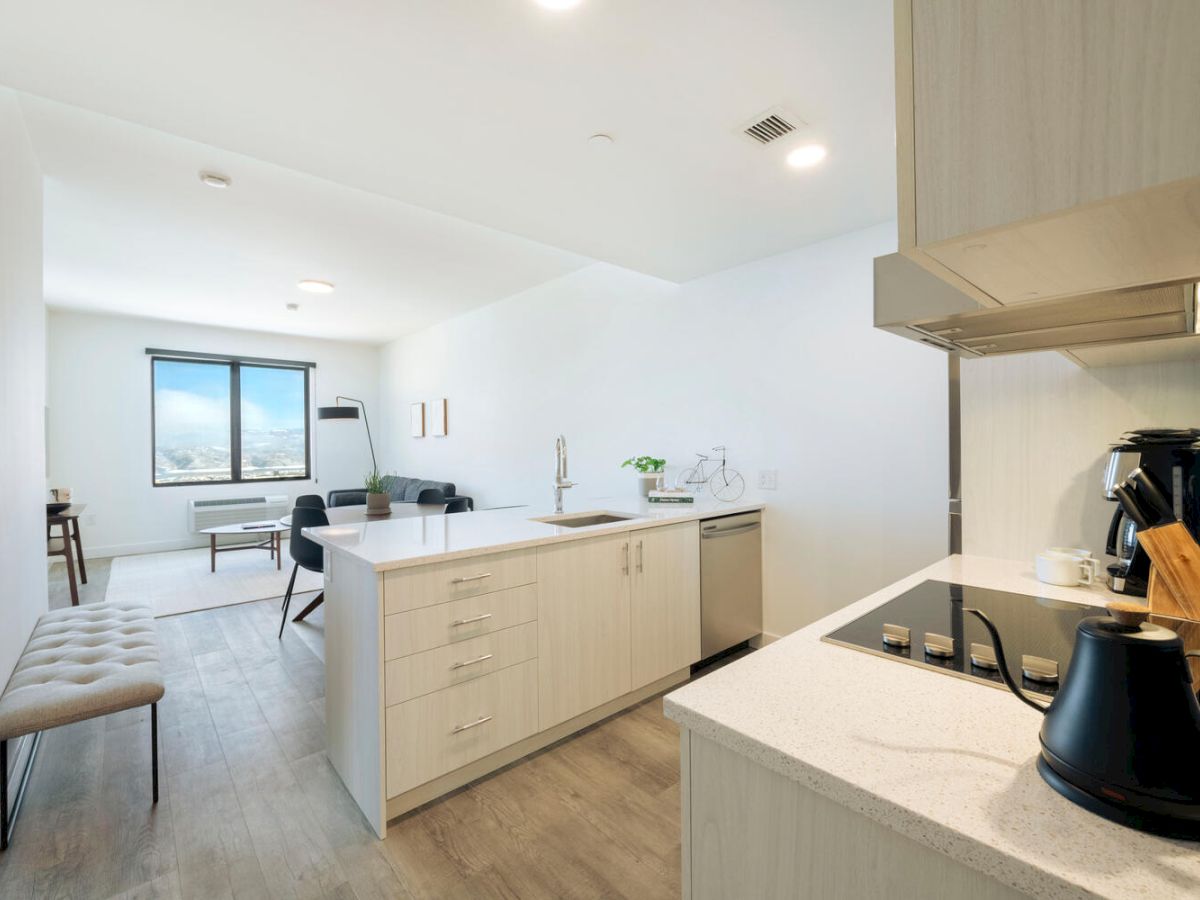 A modern kitchen with light wood cabinets, a center island, stainless steel appliances, and a view of a dining area by a window.