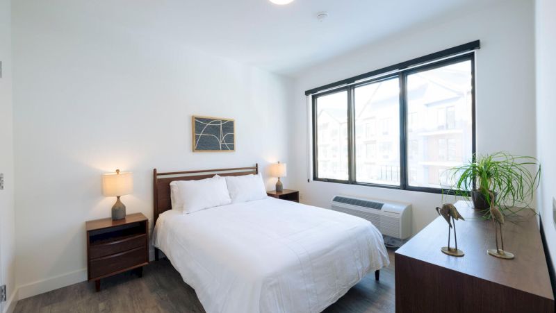 A clean and minimalist hotel room with a bed, two nightstands, a dresser, and a large window.