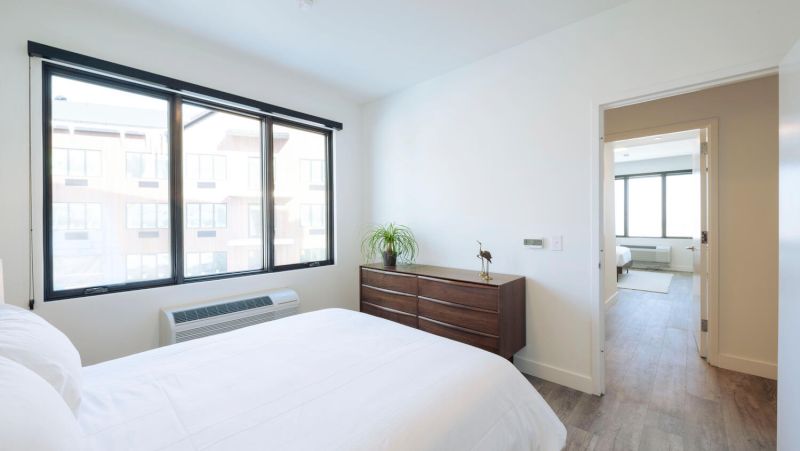 A wide view of a room with a bed, dresser, and window