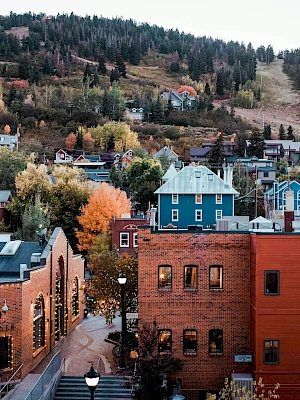 A picturesque small town with colorful houses, brick buildings, and lush autumn foliage nestled in a mountainous landscape.