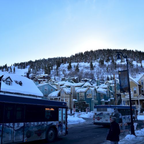 A snowy mountain town with colorful houses, buses on the street, and snow-covered trees under a clear blue sky.