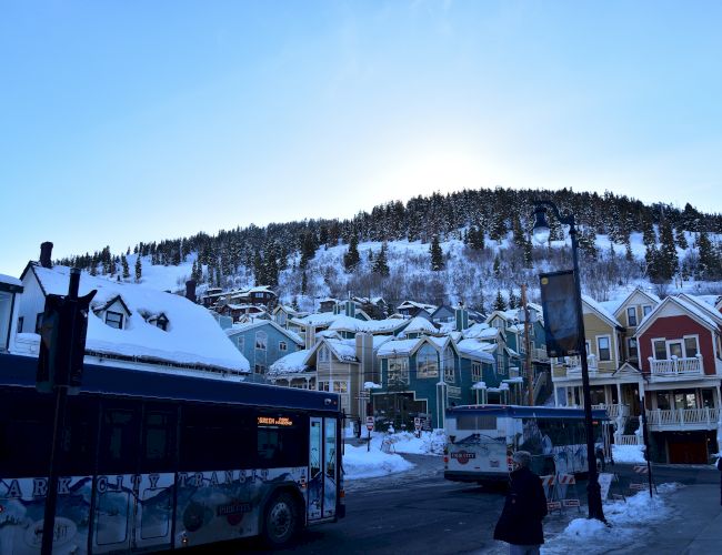 A snowy mountain town with colorful houses, buses on the street, and snow-covered trees under a clear blue sky.