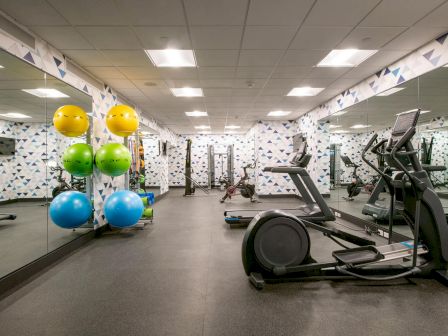 A gym room with exercise equipment, colorful exercise balls, and mirrors on the walls is shown in the photo.