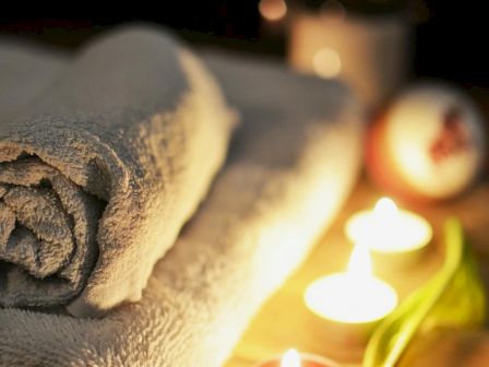 A relaxing spa setup with towels, candles, and a purple tulip on a wooden surface.