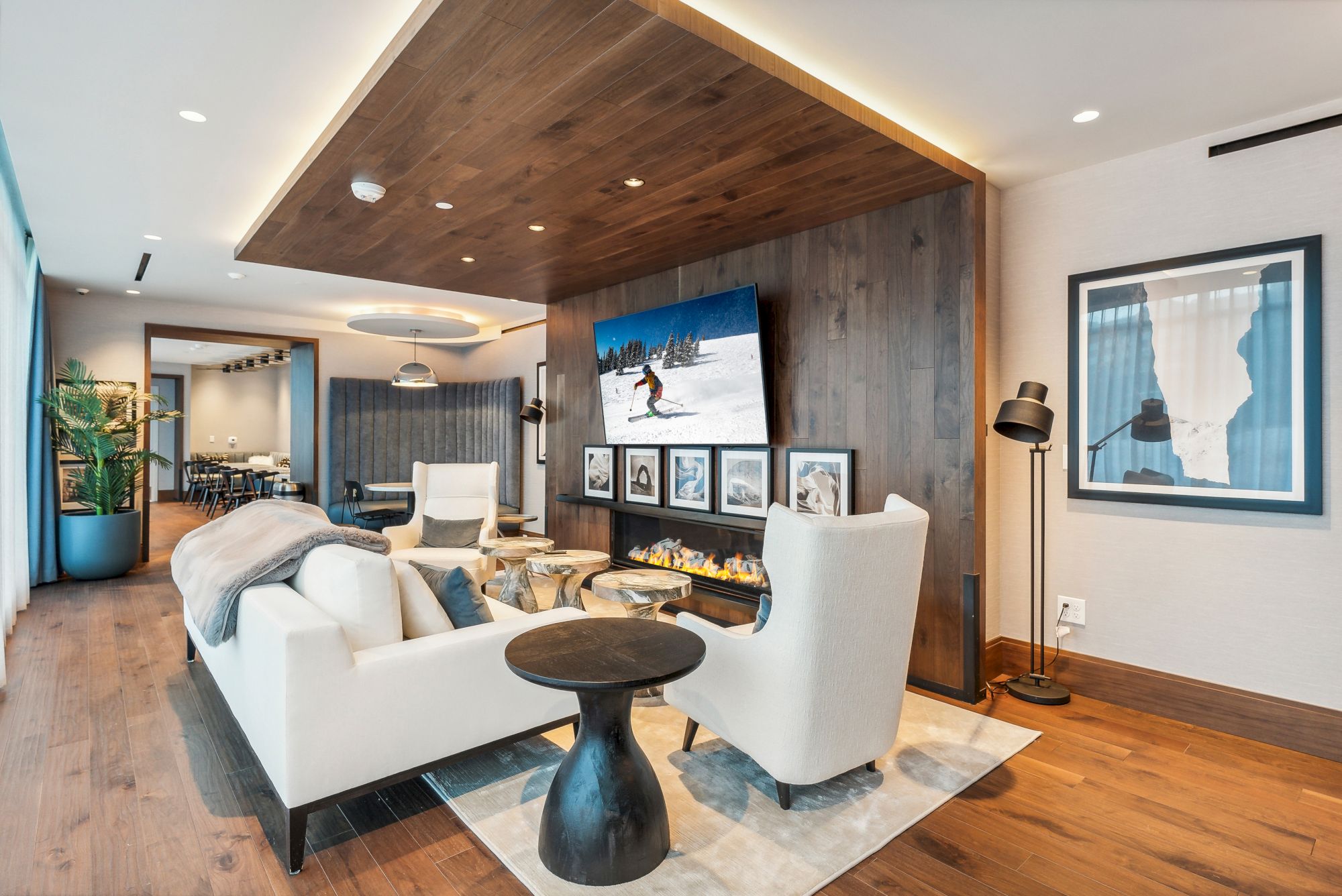 A modern living room with a cozy seating area, wall-mounted TV, and stylish decor, featuring wood accents and white armchairs.