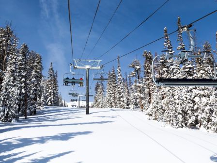 A snowy ski slope with a chairlift and snow-covered trees under a clear blue sky, ready for a day of skiing and riding.